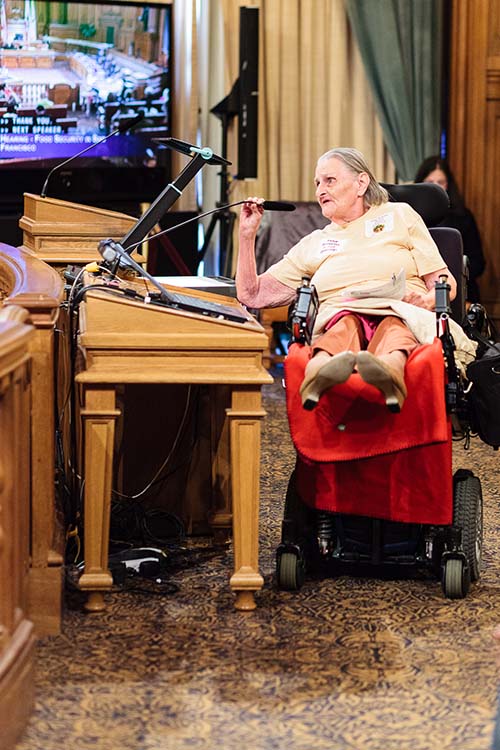 elderly woman in wheelchair speaking into microphone